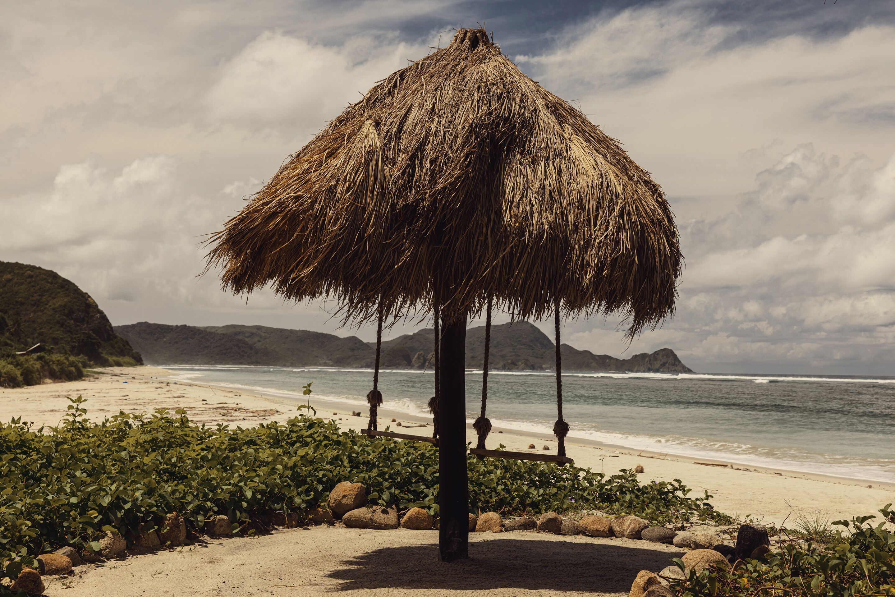 Une plage avec une structure à toit de chaume, une étendue de sable et une côte rocheuse.