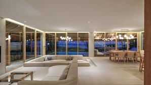 A modern living room with a large sectional sofa, a dining area with wooden furniture, and large windows offering a view of the outdoors.