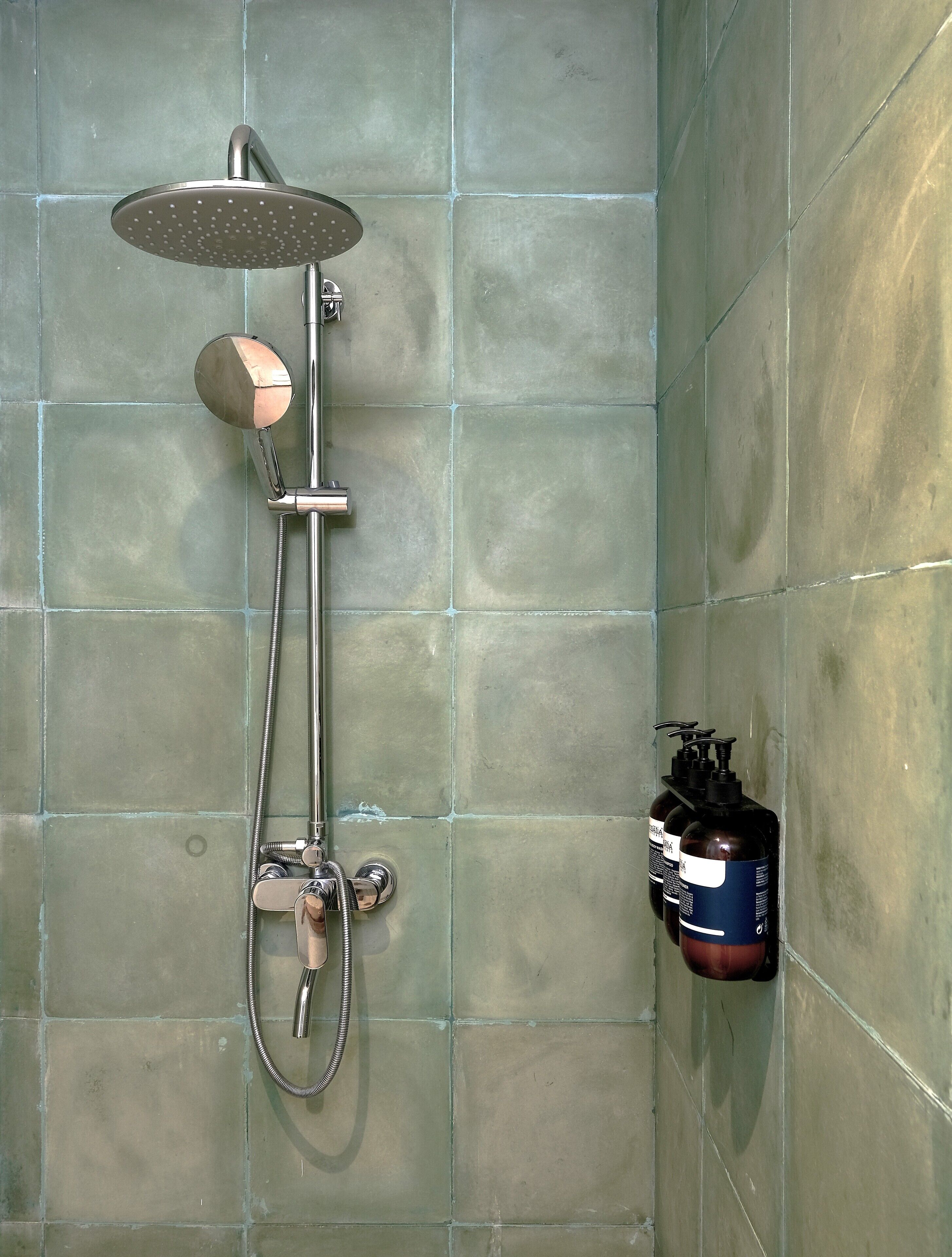 Una ducha con cabezal de ducha de lluvia y cabezal de ducha manual, una manguera para ducha manual y una botella de champú en la pared.