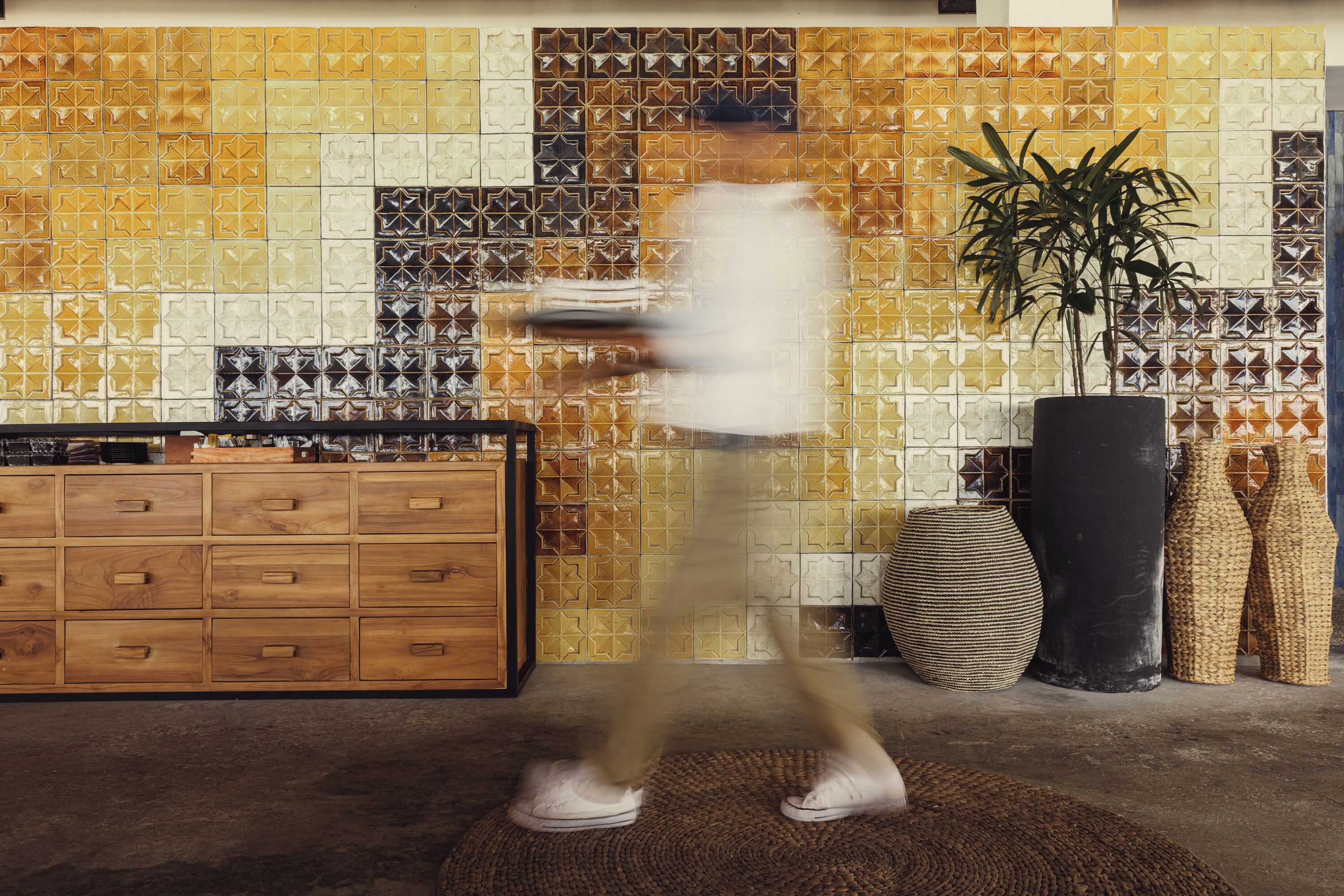 A room with a patterned tile wall, a wooden cabinet, and a large potted plant.