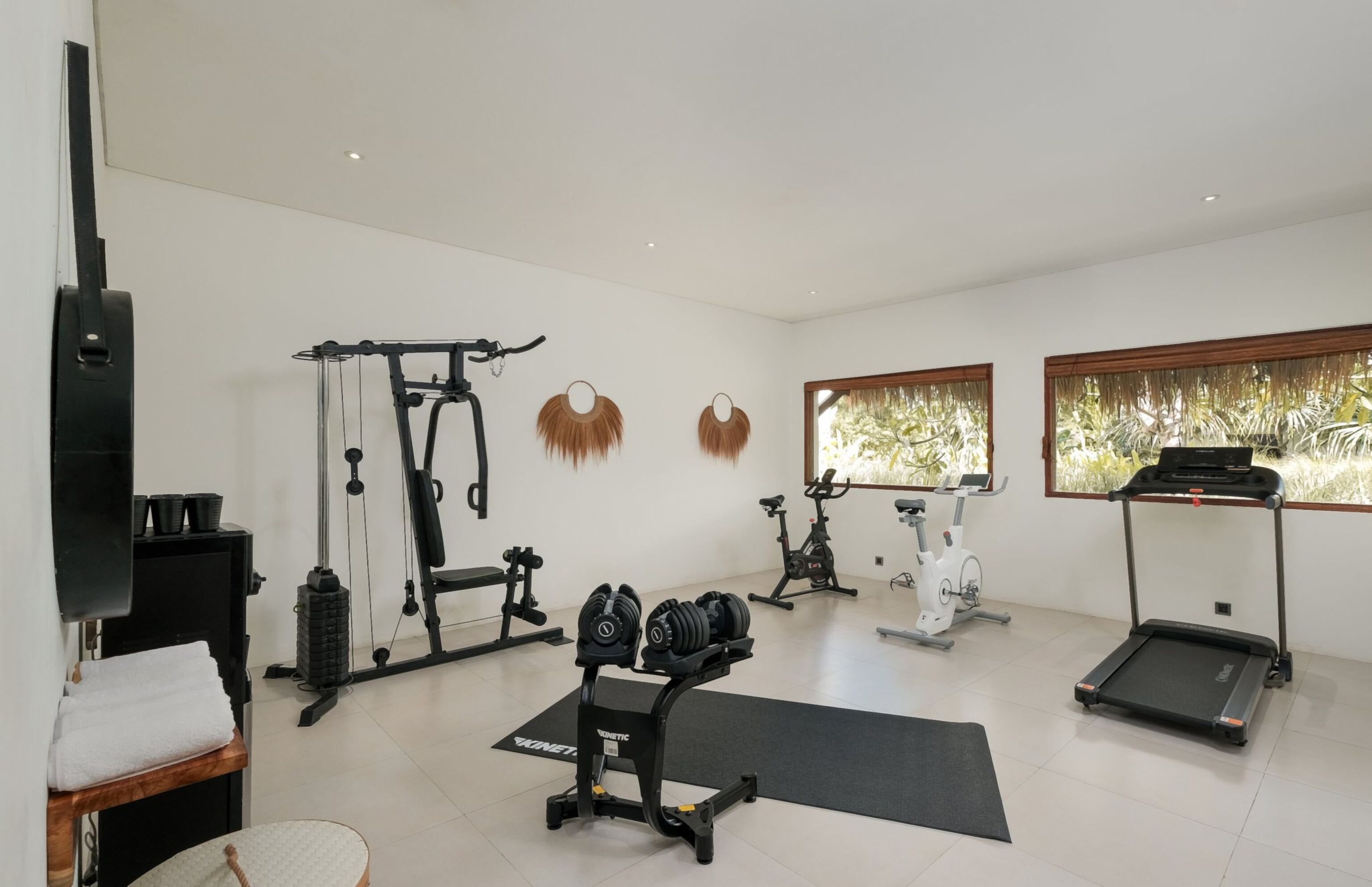 A home gym with various exercise equipment, including a treadmill, stationary bike, and weight bench.