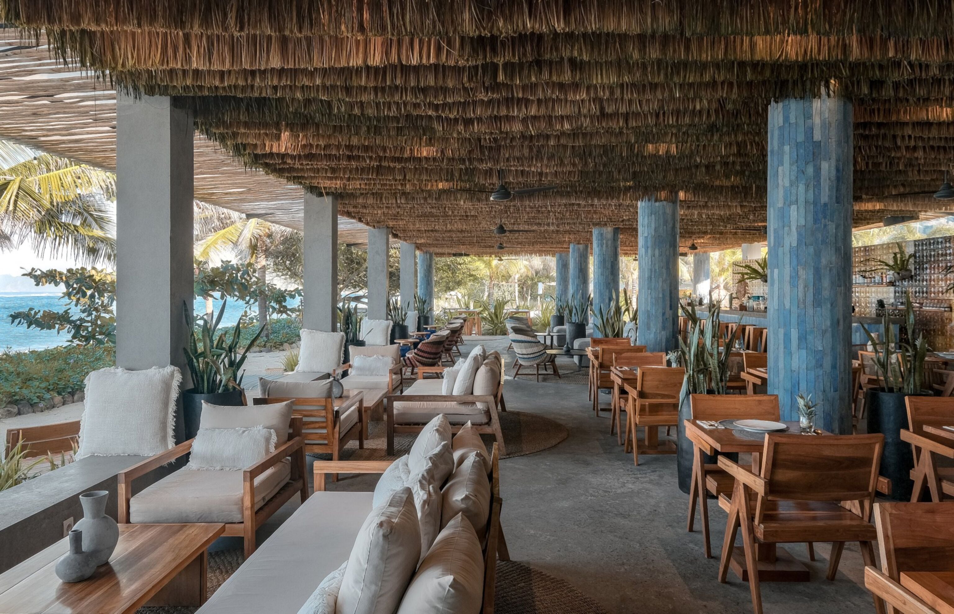 A covered outdoor seating area with wooden furniture and a view of the ocean.