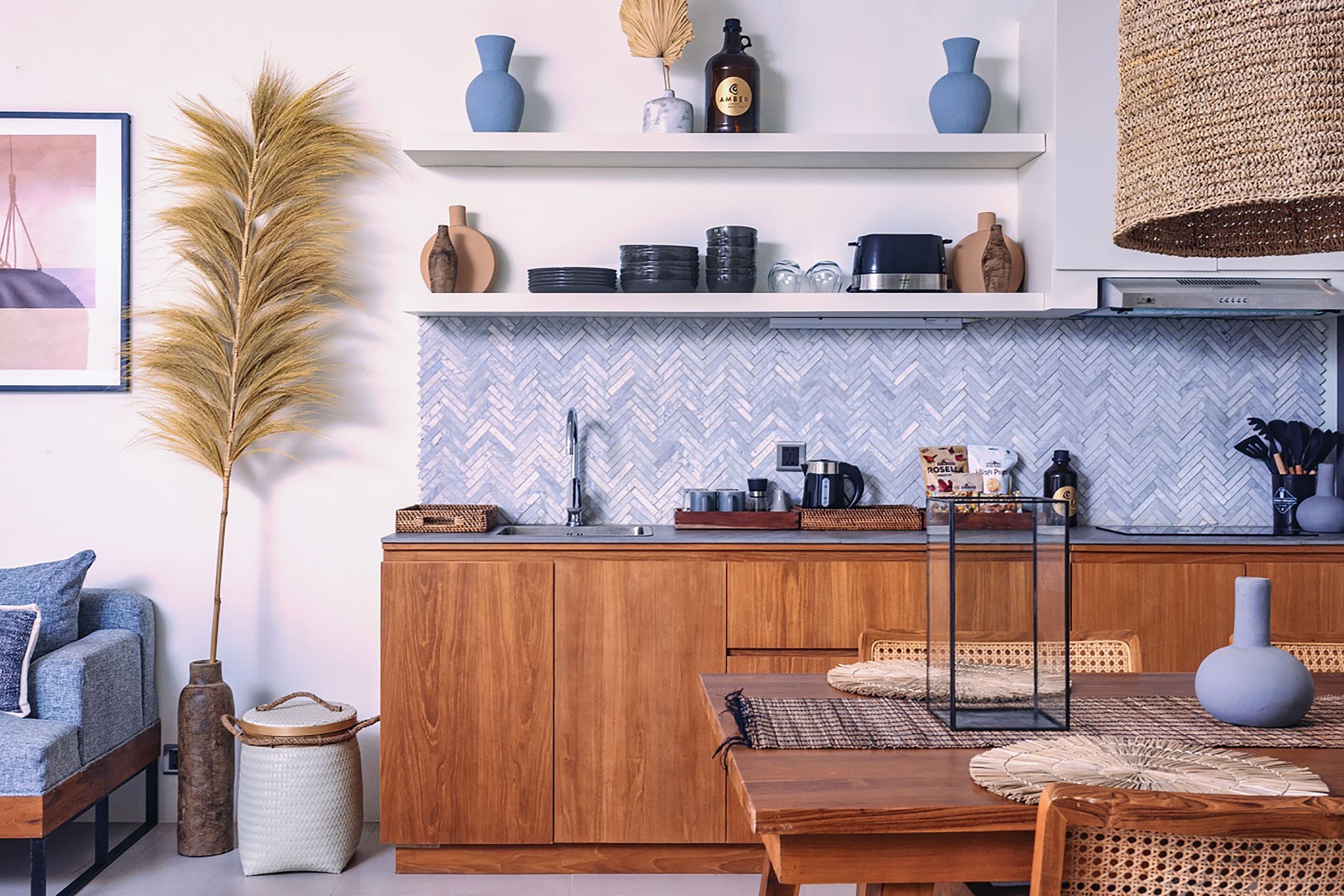 Une cuisine moderne avec des meubles en bois, un dosseret en carreaux disposés en motif chevron et un coin repas comprenant une table et des chaises en bois.