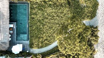 Vista aérea de un área privada con piscina, terraza de madera, sillas de descanso y una estructura de techo de paja.