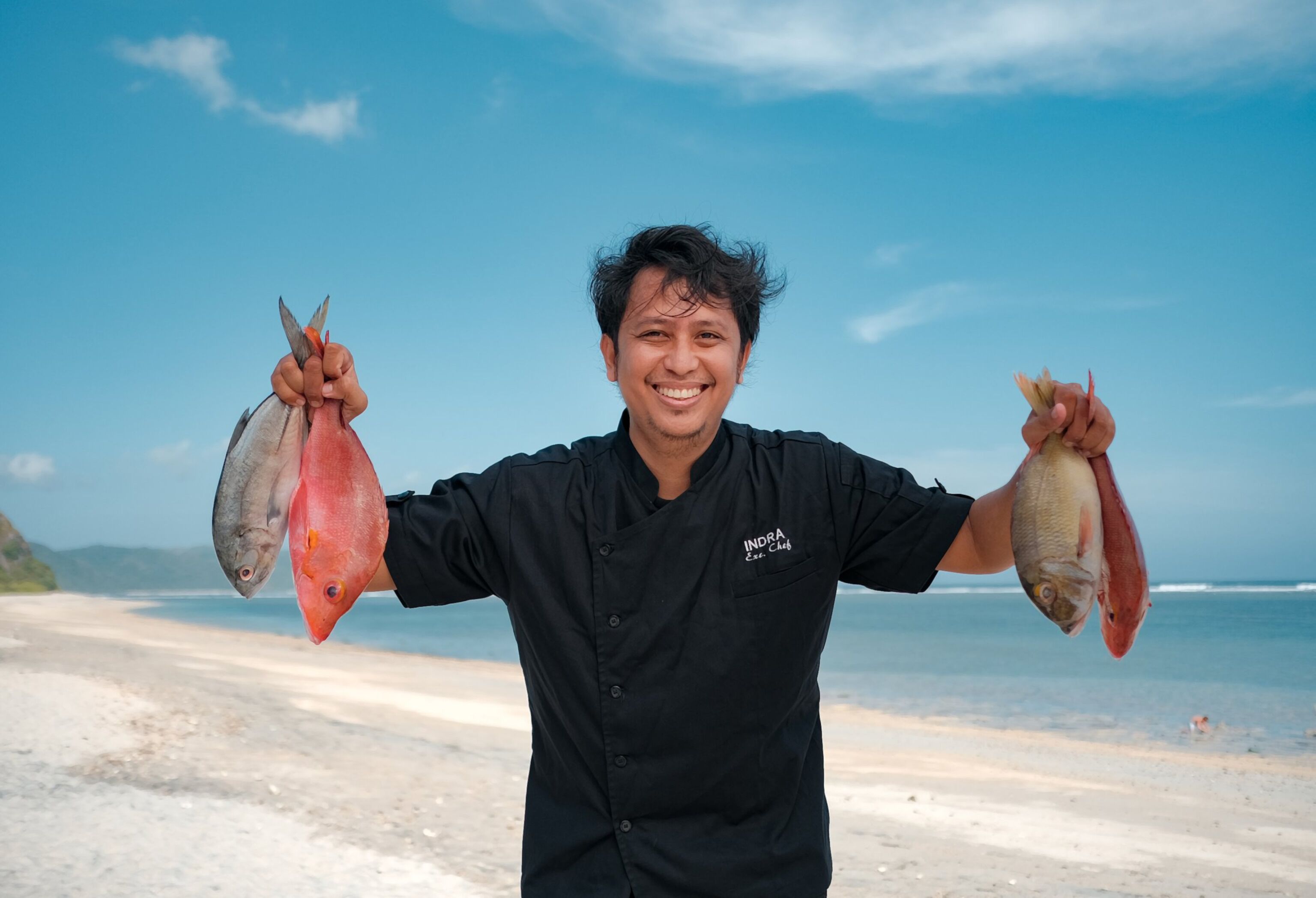 Eine Person hält zwei Fische am Strand.