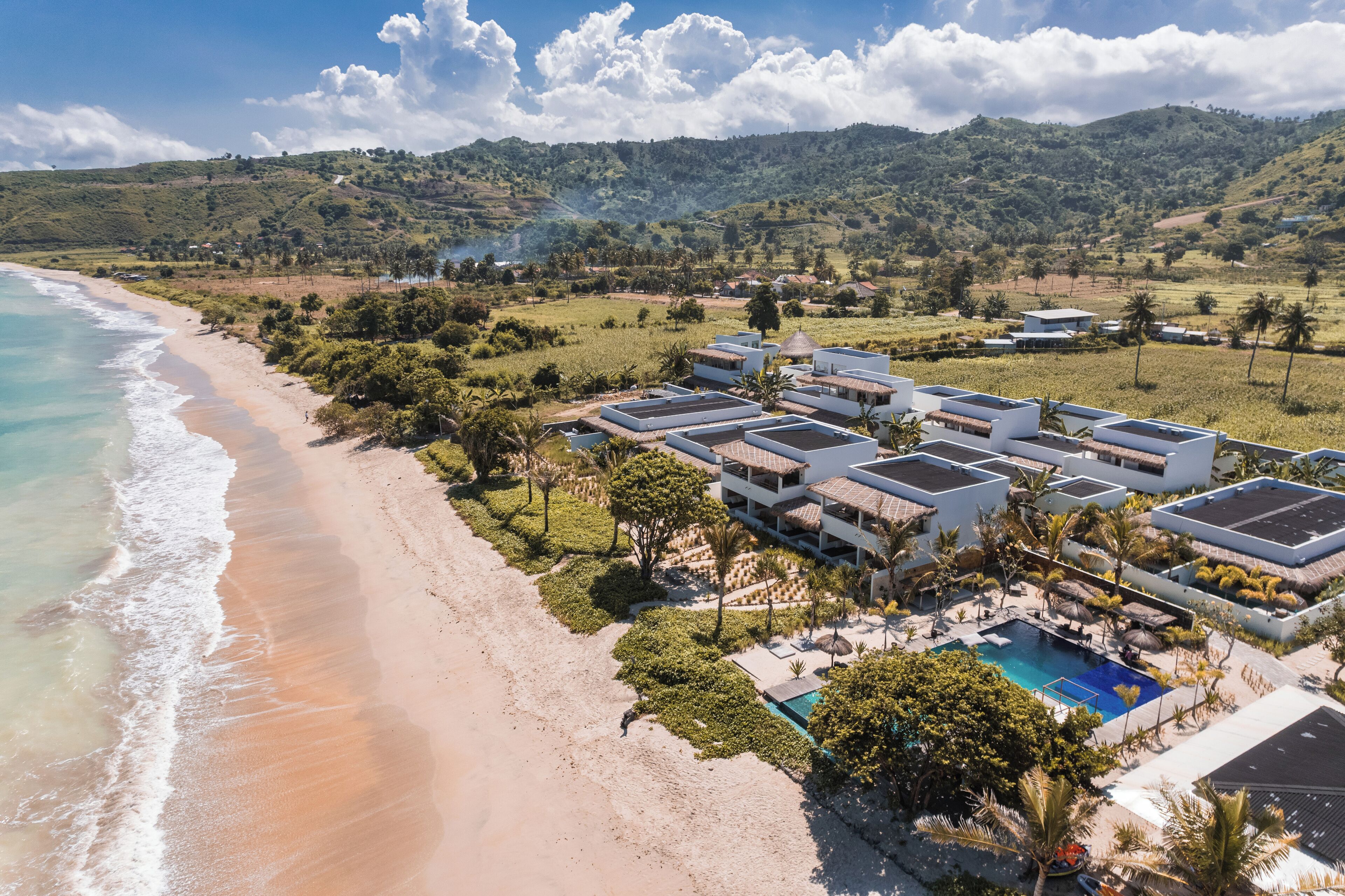 A coastal hotel with multiple buildings, a swimming pool, and a beach.