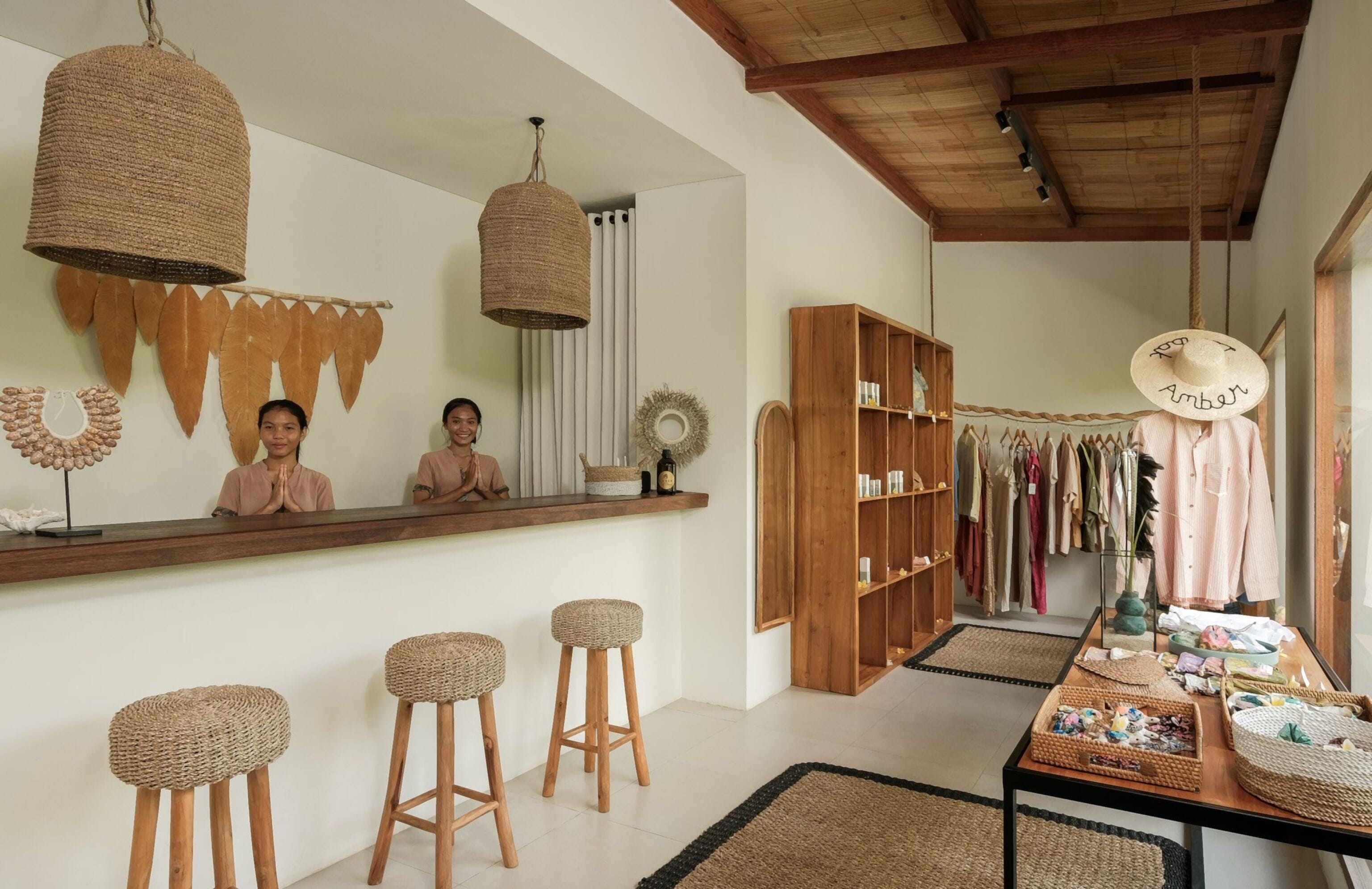 A room with a wooden bar, woven stools, a clothing rack, and a table with various items.