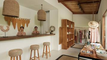 A room with a wooden bar, woven stools, a clothing rack, and a table with various items.