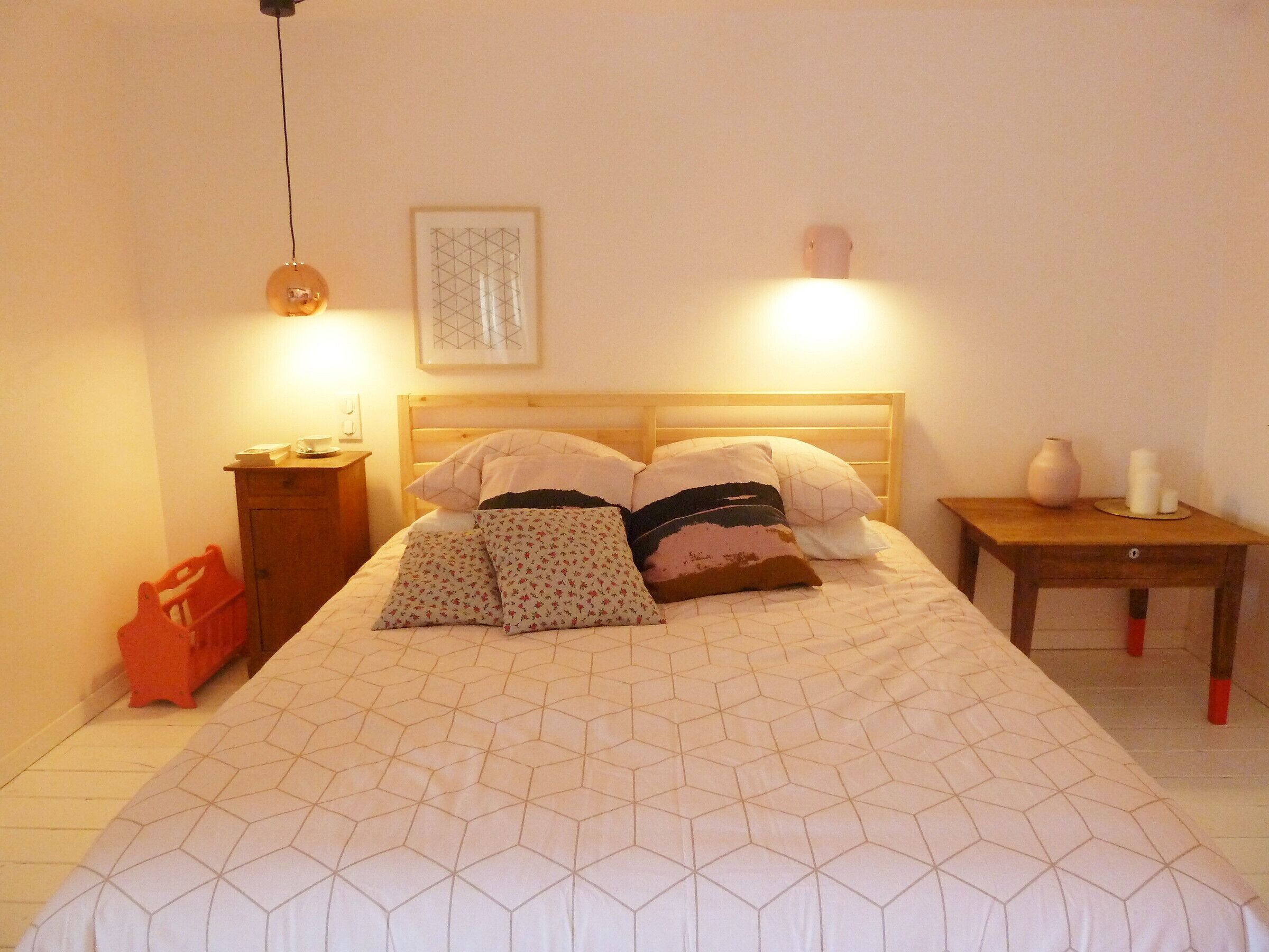 Un dormitorio con una cama de madera, una mesita de noche, un aparador y una mesilla con un florero y velas.