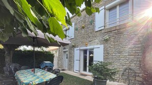 Ein Haus aus Stein mit einer überdachten Terrasse, einem Tisch mit Stühlen und einem Blumentopf.