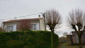 Ein Gebäude aus Stein mit einem Ziegeldach, einer Hecke davor und einem Weg, der zu einer Steinmauer führt.