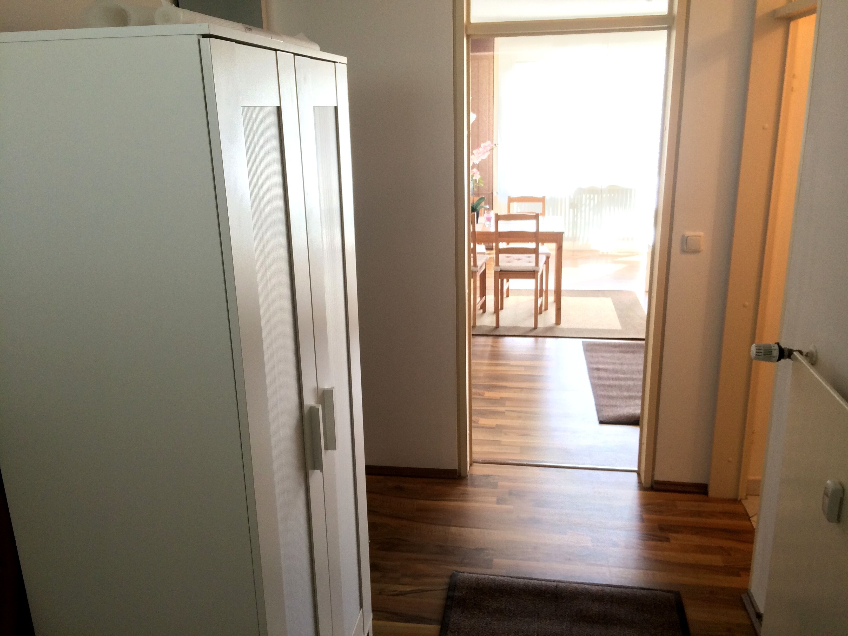 A hallway with a wooden floor leading to a dining area with a table and chairs.