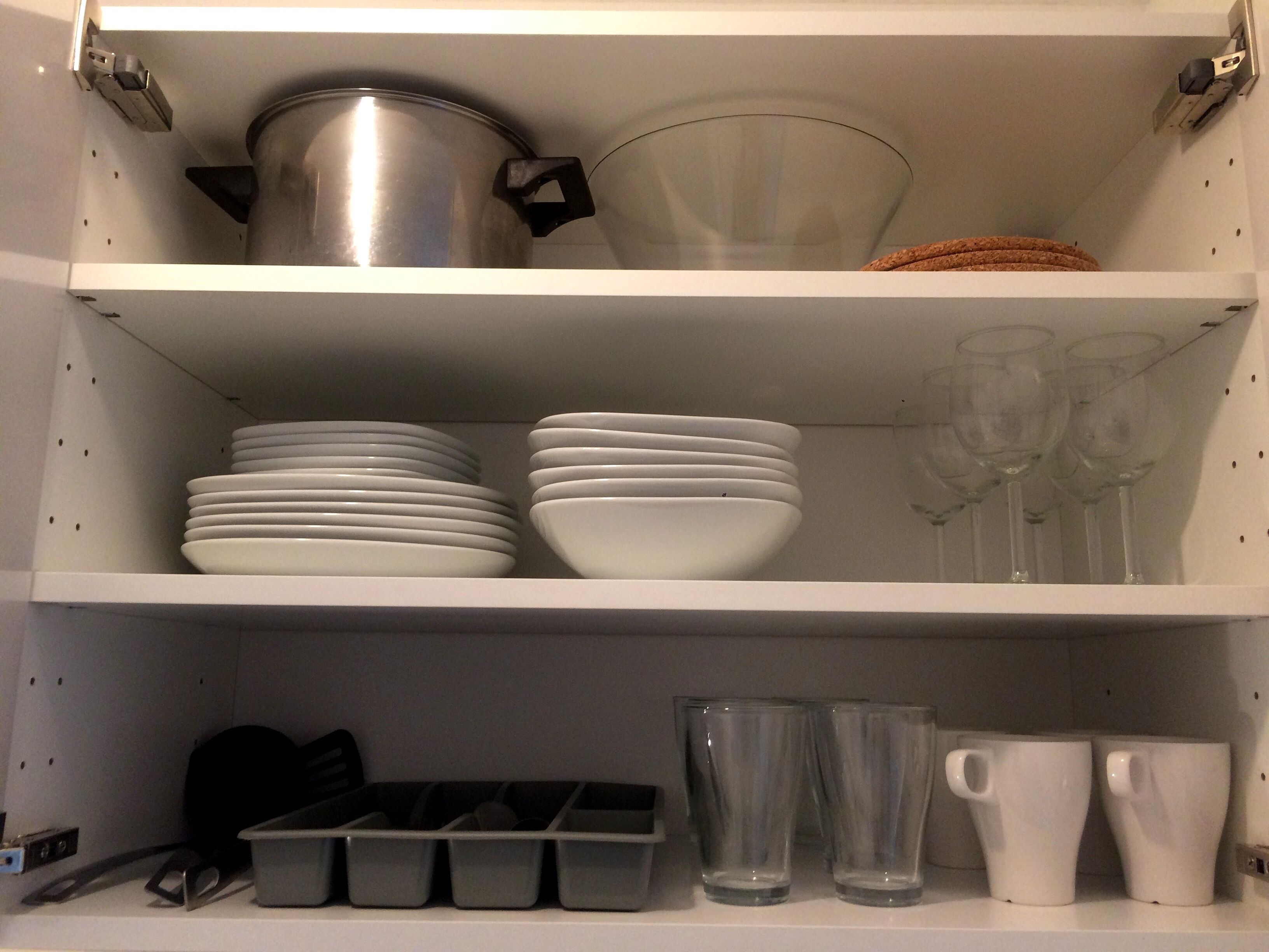 A kitchen shelf with white plates, bowls, and glasses, and a pot.