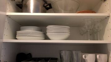 A kitchen shelf with white plates, bowls, and glasses, and a pot.