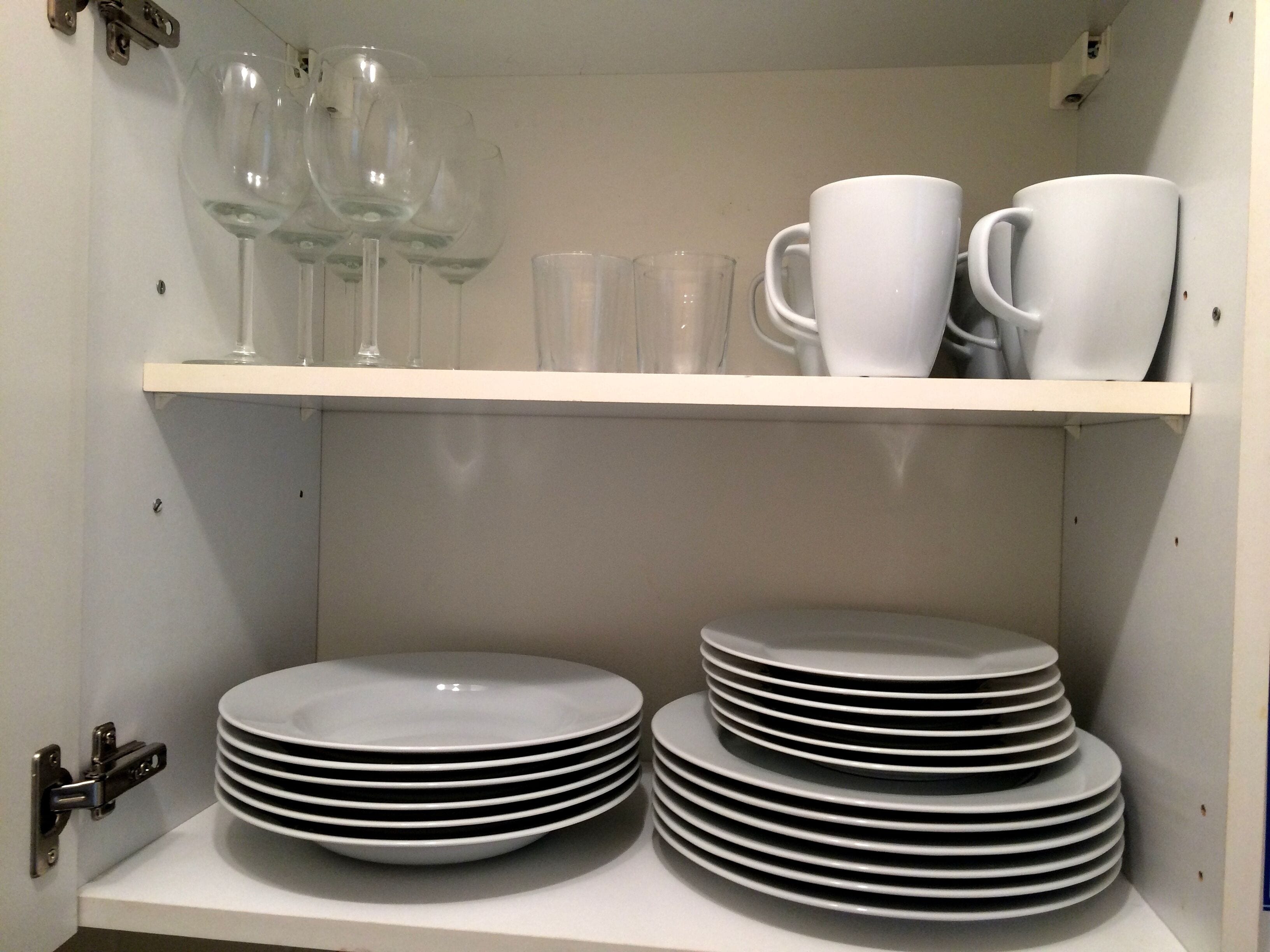 A storage area with shelves holding white plates, cups, and wine glasses.