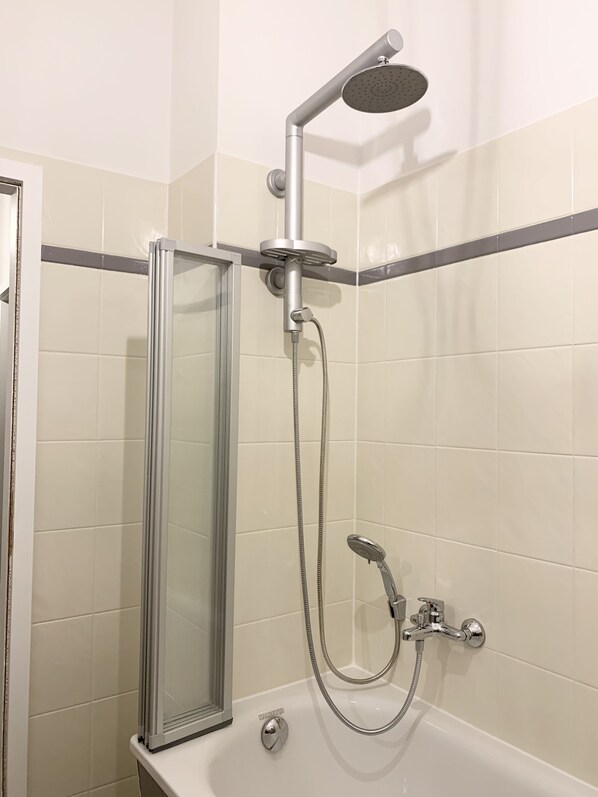 Une douche moderne dotée d’un pommeau de douche à main et d’une grande pomme de douche fixée au plafond, créant un effet de pluie.