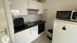 A compact kitchen with white cabinets, a black countertop, a microwave, and a small trash bin. - Studio 100m from the Sea in Saint-Hilaire-de-Riez, with Balcony and Public Parking (Saint-Hilaire-de-Riez)