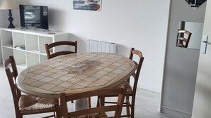 A dining area with a round table, four wooden chairs, a white cabinet with a television, and a framed picture on the wall. - Studio 100m from the Sea in Saint-Hilaire-de-Riez, with Balcony and Public Parking (Saint-Hilaire-de-Riez)