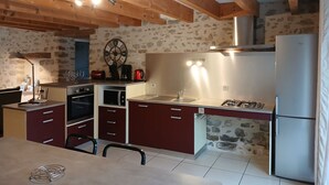 A kitchen with wooden beams, a stone wall, a clock, a stove, and a refrigerator.