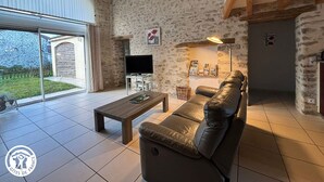 A spacious living room with a large window, a leather sofa, a wooden coffee table, and a television on a stand.