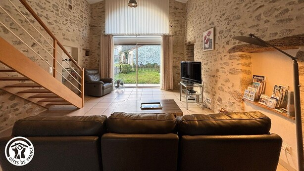 A spacious living area with a stone wall, a wooden staircase, a leather sofa, a TV, and a bookshelf.