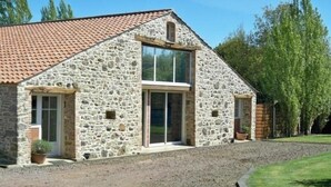Un bâtiment en pierre avec un toit en tuiles, une grande porte vitrée et une allée gravillonnée.