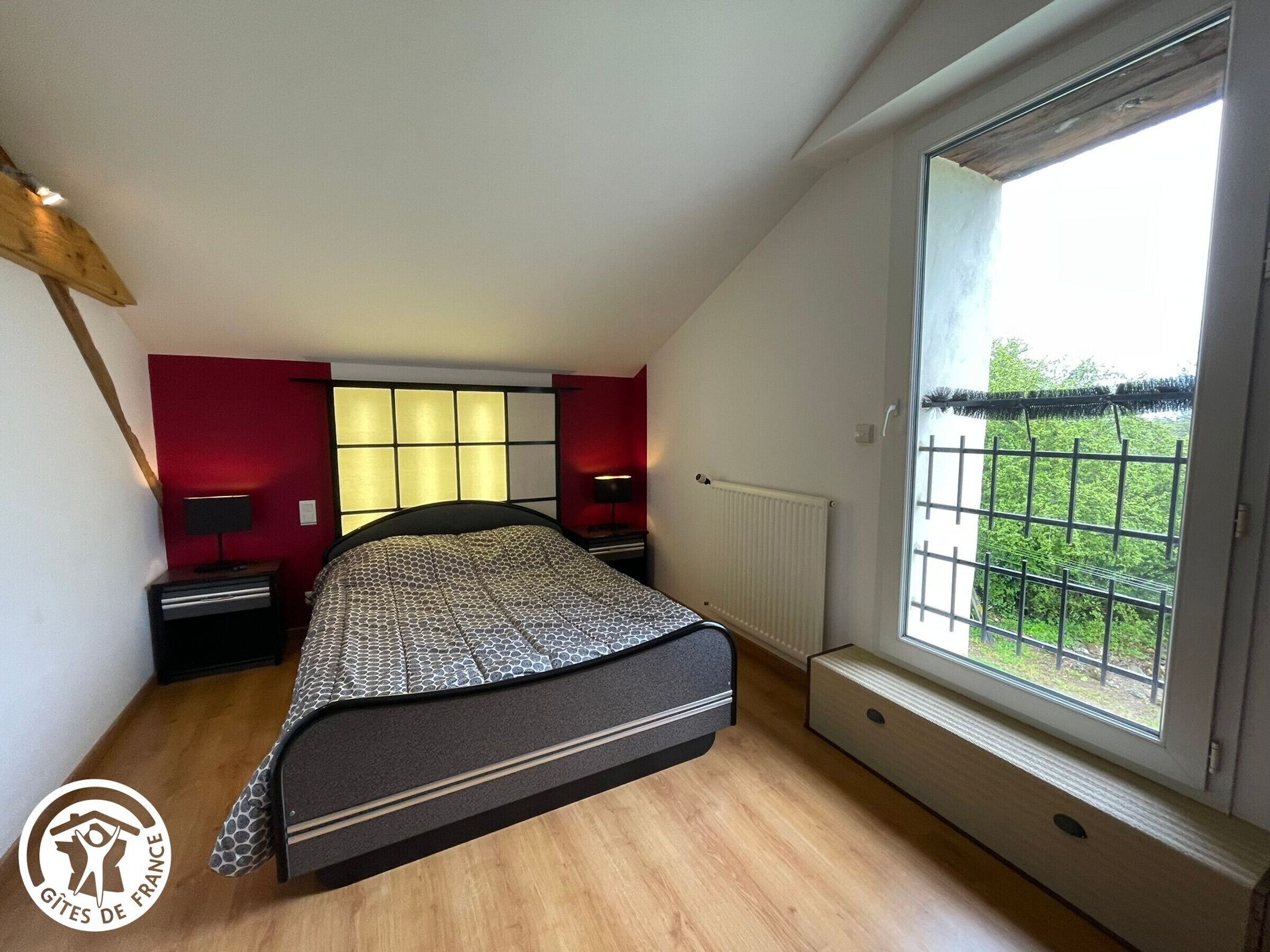 Un dormitorio con cama, ventana con vistas, radiador y mesita de noche.