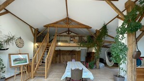 Un intérieur rustique avec un escalier en bois, une table à manger recouverte d’une nappe à motifs et des plantes en pot.