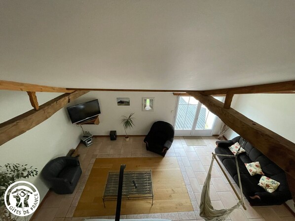 Un dormitorio estilo loft con techo de madera, un televisor montado en la pared, un sofá negro, una mesita pequeña y un sillón colgante.