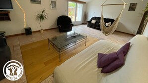 Un grand espace de vie comprenant un canapé, un fauteuil suspendu, une table basse et un téléviseur.