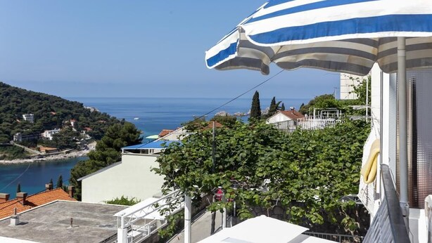 A coastal view with a blue and white striped umbrella, a clear sky, and buildings along the shoreline. - Lapad View (Dubrovnik)