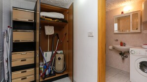 A laundry room with a washing machine, a sink, and a mirror above it. There is a wooden shelf with a towel and a vacuum cleaner. - Lapad View (Dubrovnik)