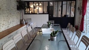 A dining area with a glass table, white chairs, and potted plants.