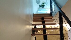 A wooden staircase with a black handrail, leading to a lower level with a stone wall and a white dresser with a vase of flowers.