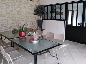 A dining area with a glass table, white chairs, a red pot with a plant, and a decorative tray. - Family Retreat with Heated Pool, Near Puy du Fou & La Rochelle, Sleeps 14 (L'Hermenault)