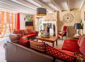 A cozy living room with a brown sofa, red cushions, a wooden coffee table, and a stone wall. - Family Retreat with Heated Pool, Near Puy du Fou & La Rochelle, Sleeps 14 (L'Hermenault)