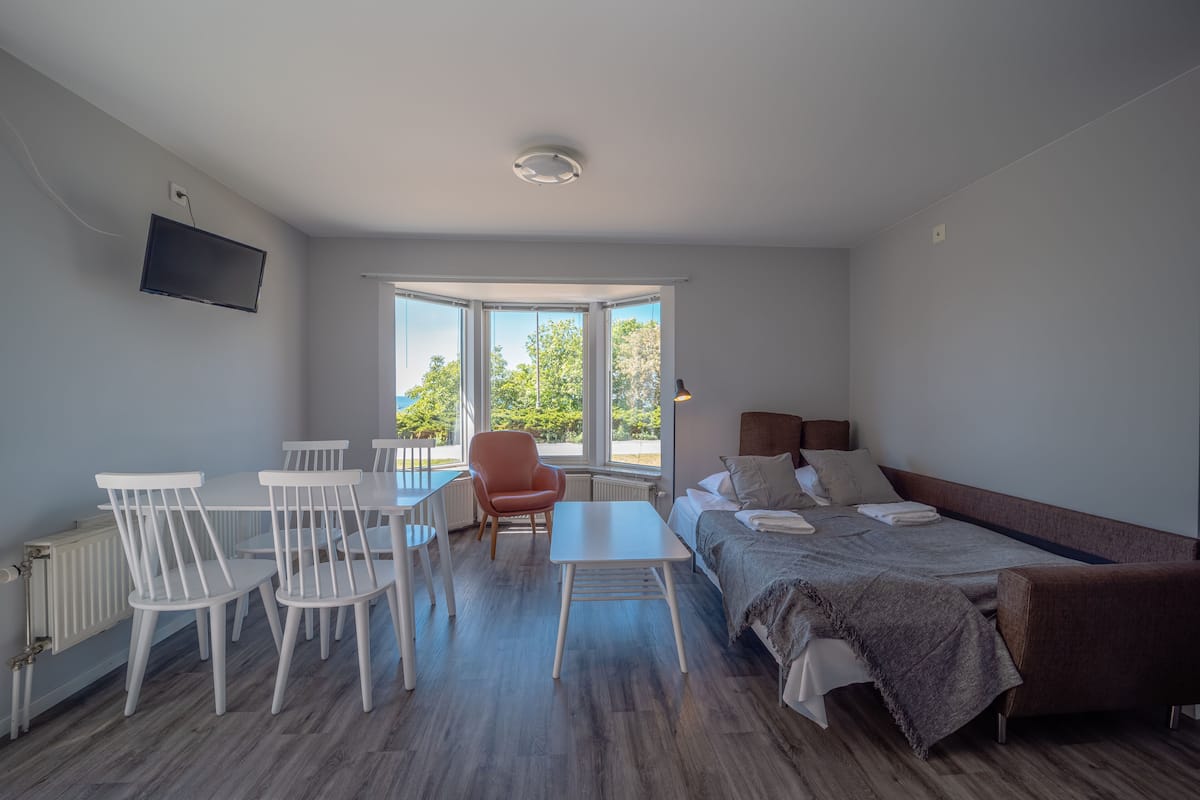 A modern bedroom with a bed, a desk, and chairs. There is a window providing natural light.
