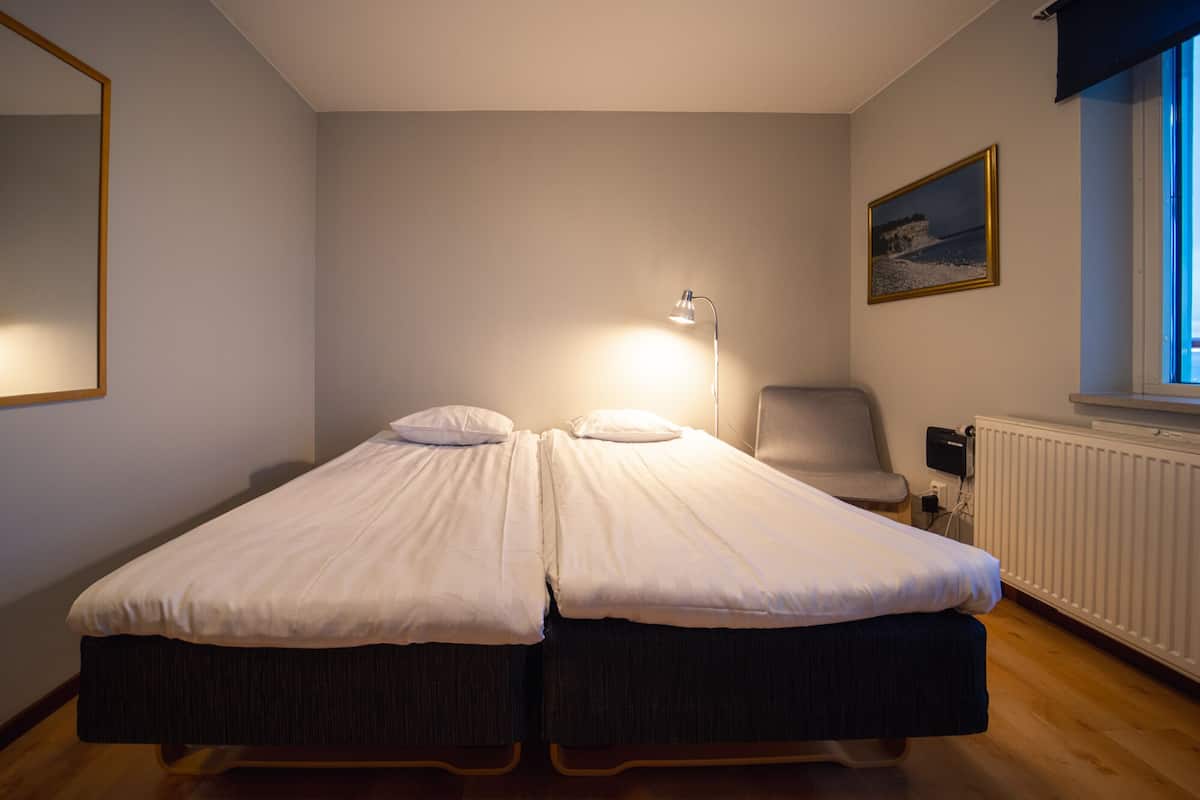 A twin bed with a single pillow, a bedside lamp, a chair, and a window with a view of cliffs.