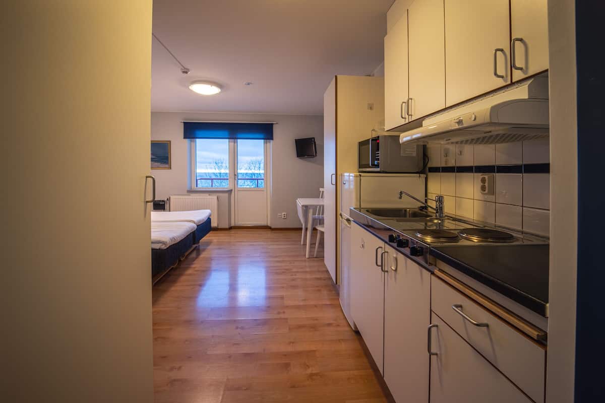 A compact kitchen with a microwave, stove, and sink. There is a small dining area with a table and chairs, and a window with a view of trees.