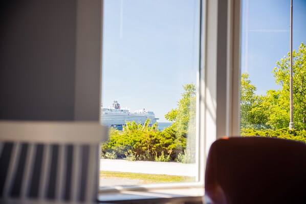 Blick auf ein Kreuzfahrtschiff durch ein Fenster mit Blick auf eine begrünte Fläche mit Bäumen.