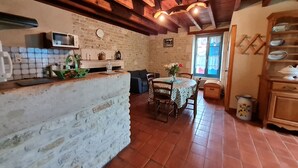 A rustic kitchen with exposed wooden beams, a stone wall, and a tiled floor.