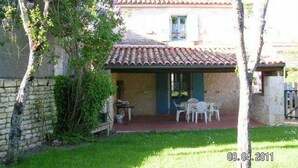 A rustic stone building with a tiled roof, a small patio with outdoor seating, and a date stamp of 08.04.2011.