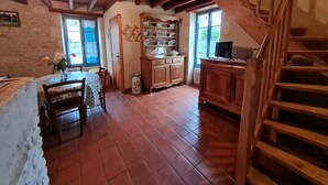 A rustic interior with a wooden staircase, a dining area with a table and chairs, and a kitchen area with cabinets and a shelf.