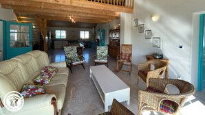 Un vaste espace de vie doté d’un haut plafond, d’un balcon, d’un ensemble de canapés, de fauteuils en osier et d’une table à manger.