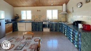 Une cuisine avec un plafond en bois, un dosseret carrelé et un coin repas agrémenté d’une nappe à motifs.