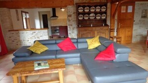 A living room with a blue sectional sofa, a wooden coffee table, and a kitchen area in the background. - Charming Cottage with Private Pool, Sauna, and Garden in Saint-Juire-Champgillon (Saint-Juire-Champgillon)