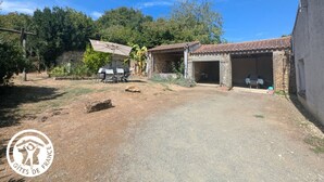 A rustic property with a dirt driveway, a patio with outdoor seating, and a stone building with a tiled roof. - Charming Cottage with Private Pool, Sauna, and Garden in Saint-Juire-Champgillon (Saint-Juire-Champgillon)