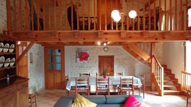 A spacious living area with a blue sofa, wooden staircase, and a dining table set for four. - Charming Cottage with Private Pool, Sauna, and Garden in Saint-Juire-Champgillon (Saint-Juire-Champgillon)