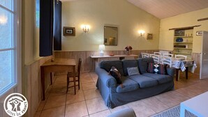 A cozy living room with a sofa, a dining table, and a kitchen area. - Charming Renovated House with Private Pool in Saint-Christophe-du-Ligneron (Saint-Christophe-du-Ligneron)