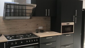 Et moderne køkken med sorte skabe, en rustfri emhætte, indbygget ovn og en bordplade med kaffemaskine.